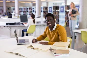 Portrait of smiling african-american male student with laptop and book in public library. High quality photo