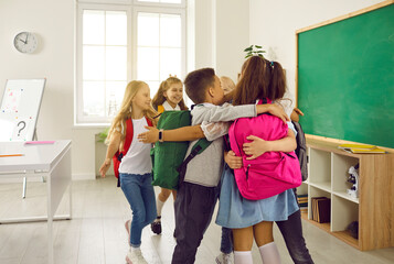 School friendship. Joyful elementary school students gather in circle and hug at school before classes. Friendly classmates with backpacks on their shoulders are having fun and greeting each other.