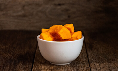 Sliced pumpkin in a white bowl on a wooden table.