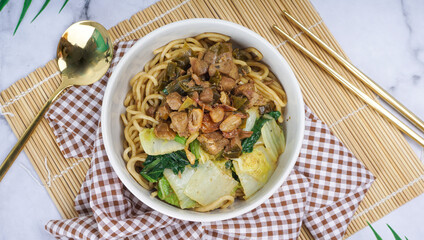 Top view of Mie Ayam as Indonesia chicken noodles topped with diced chicken, green vegetables and chili sauce in white background