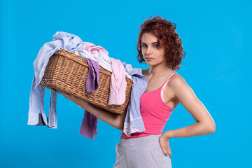 A disgruntled girl stands with a wicker basket full of clothes to wash.