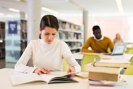 Portrait of confident woman with book in public library. High quality photo
