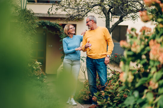 Senior couple holding keys and standing outside their new home