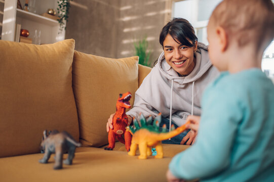 Mother and toddler son playing with dinosaurs toys at home on the couch