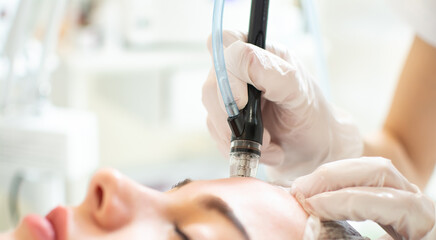 Closeup shot of young woman receiving microdermabrasion therapy on forehead at beauty spa