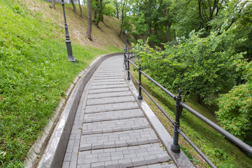 Paved path with railings on hillside in summer city park