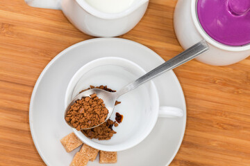 Instant coffee granules in spoon atop empty cup, top view