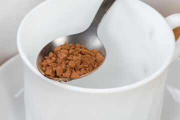 Instant coffee granules in spoon atop empty cup close-up