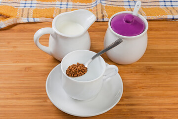 Instant coffee granules in spoon atop empty cup on table