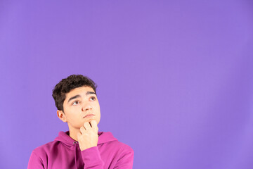 Portrait of hispanic boy thinking and looking at copy space isolated on purple background