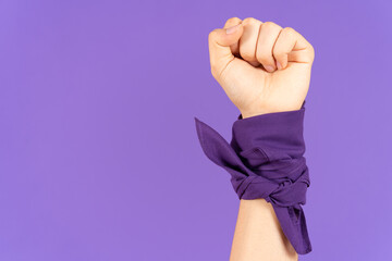 Closeup of closed fist and kerchief tied on wrist isolated on purple background. Feminism and protest concept with copy space - obrazy, fototapety, plakaty