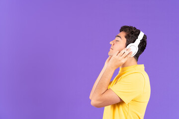 Hispanic teenager boy listening to relaxing music on headphones isolated on purple background with copy space