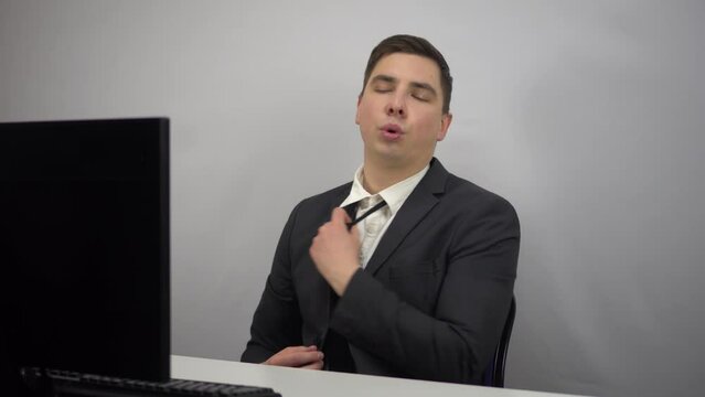A young businessman is working hard and is now relaxed. A man in a suit has loosened his gauntlet and is resting while sitting in the office at the PC.