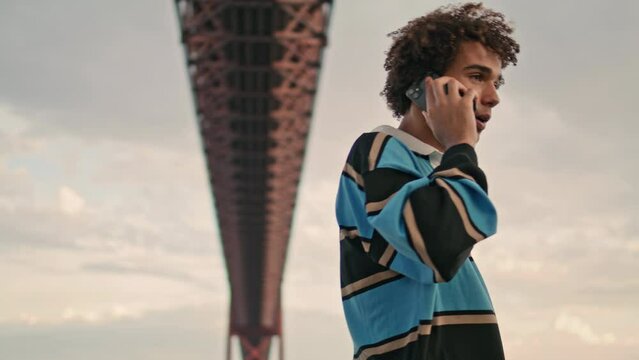 Serious zoomer calling phone cloudy day closeup. Millennial guy talking mobile