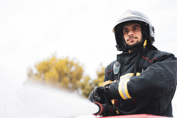 A young firefighter dressed in uniform uses the hose to put out a fire, emergency service.