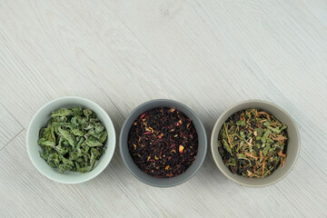 Variety of herbal teas in bowls on a light wooden background. Set of aromatic leaf. Flat lay.