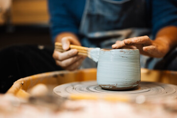 Fototapeta na wymiar Close up on skillful male hands making and sculpting pottery jar on potter’s wheel with tools and water in workshop, Creative and artwork, Handmade craft.