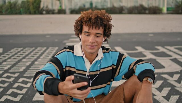 Smiling zoomer shooting smartphone street closeup. Earphones guy listening music