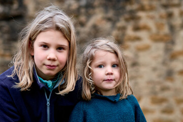 soeurs blondes jolies, 4 et 10 ans, portrait sur fond de mur de pierre