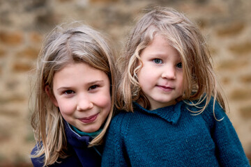 soeurs blondes jolies, 4 et 10 ans, portrait sur fond de mur de pierre