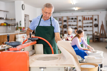 male potter professionally works with machine clay press roller for making clay blanks