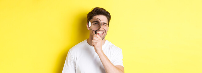 Close-up of young man looking through magnifying glass and smiling, searching something, standing...