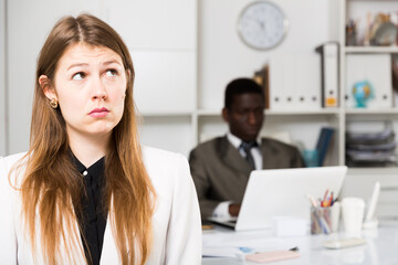 Fototapeta premium Offended woman standing at office on background with working coworker