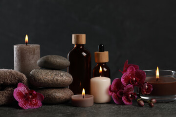 Beautiful composition with burning candles, spa stones and different care products on dark grey table