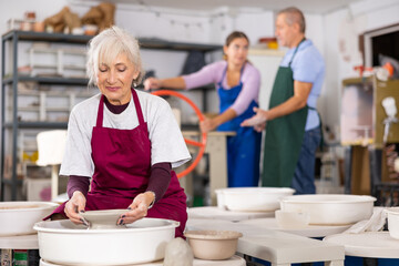 Mature woman learning how to create pottery on potter wheel in a workshop