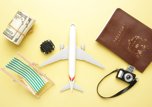A flatlay picture of aeroplane, beach folding chair, roll of fake money, suitcase, toy camera and passport on yellow background. Vacation plan concept.