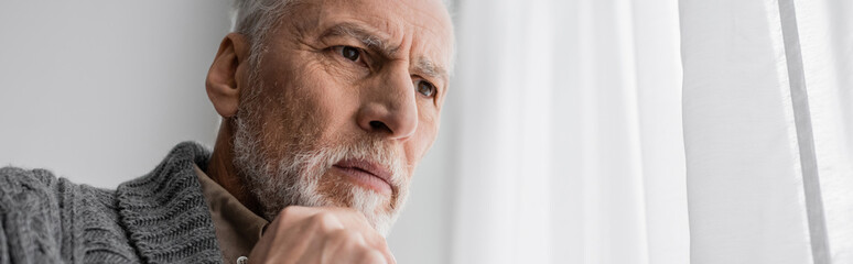 bearded senior man with alzheimer syndrome holding hand near chin and looking away at home, banner. - obrazy, fototapety, plakaty