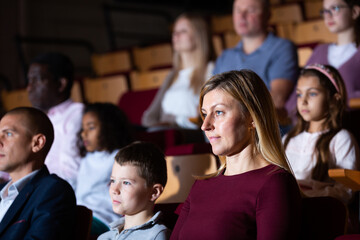 Portrait of interested woman theatergoer absorbedly watching stage performance in theater - obrazy, fototapety, plakaty