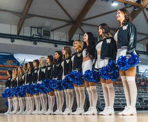 Bottom view of cheerleading team in black and white uniforms standing in line and holding blue...