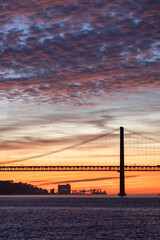 Lisbon 25th of April Bridge at sunset and industrial cranes at the background