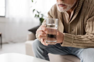 partial view of senior man with parkinson disease holding glass of water in trembling hands.