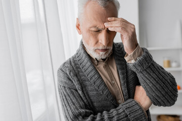 depressed senior man with alzheimer syndrome standing with closed eyes and touching forehead at...