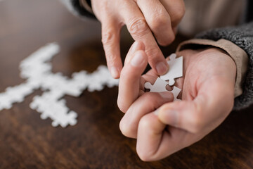 Fototapeta premium partial view of aged man with parkinson syndrome holding elements of jigsaw puzzle in trembling hands.