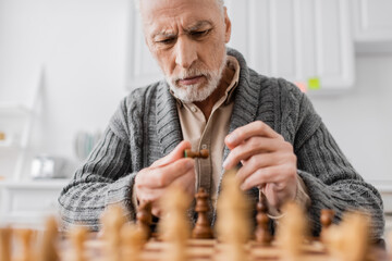 tensed man with alzheimer syndrome looking at chess figure near chessboard on blurred foreground.