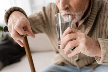 partial view of senior man with parkinsonism and tremor in hands drinking water at home.