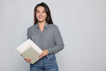 Happy young teacher with books on light grey background. Space for text