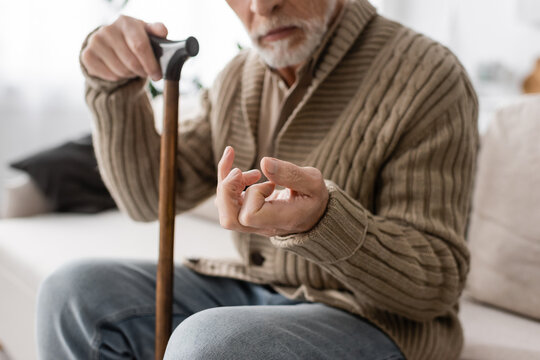 cropped view of senior man with parkinson disease holding walking cane while sitting on couch at home.