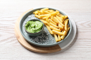 Tray with plate of french fries, salt and avocado dip on white wooden table