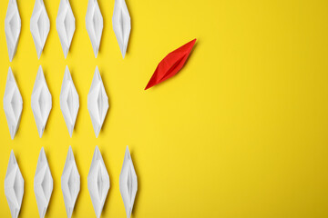 Red paper boat floating away from others on yellow background, flat lay with space for text. Uniqueness concept