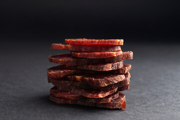 Stack of delicious beef jerky on dark table, closeup