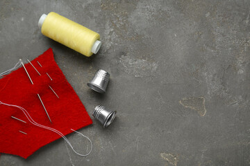 Thimbles, needles and thread on grey table, flat lay with space for text. Sewing accessories