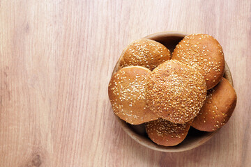 Bowl of fresh buns with sesame seeds on wooden table, top view. Space for text