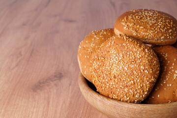 Bowl of fresh buns with sesame seeds on wooden table, closeup. Space for text