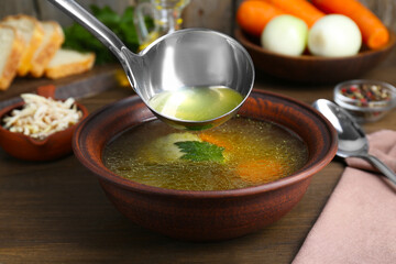 Pouring delicious chicken bouillon into bowl on wooden table, closeup