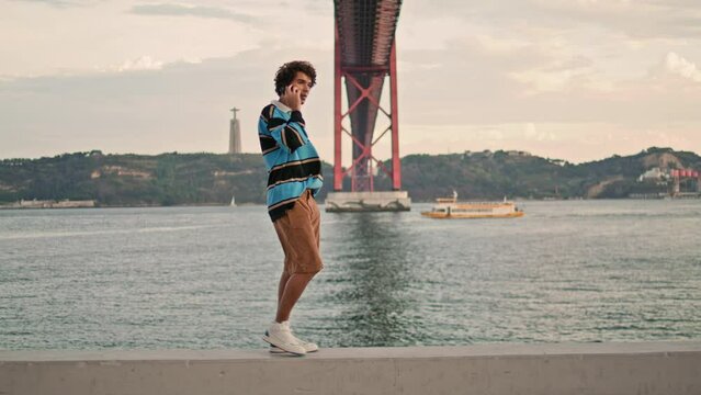 Relaxed tourist speaking smartphone Lisbon embankment. Curly guy talking mobile