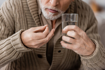 partial view of senior man with parkinson disease holding pill and glass of water in trembling...